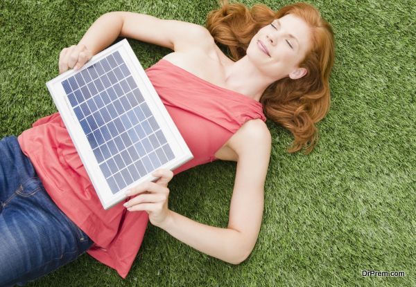 Beautiful woman lying on grass while holding solar panel