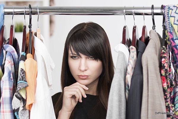Beautiful young confused woman near rack with clothes. Nothing to wear concept