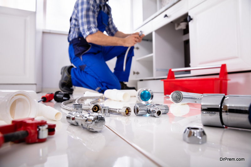 Plumber Tools And Equipment On Floor In Kitchen With Plumber Installing The Sink At Background