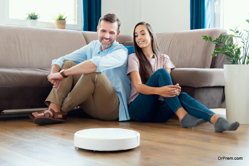Robotic vacuum cleaner cleaning the room, smiling couple sitting on the floor. Smart home concept